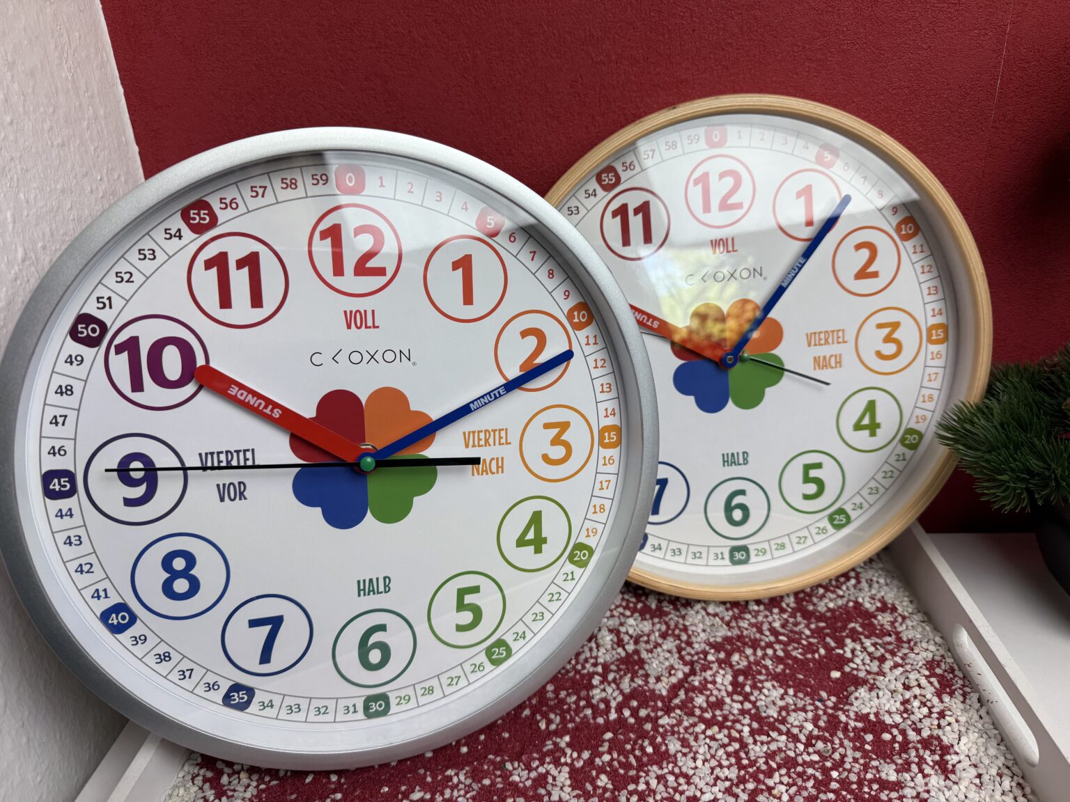 Die Cloxon Kinderuhr zum lernen der Uhrzeit, einmal in Silber und einmal in Holzoptik